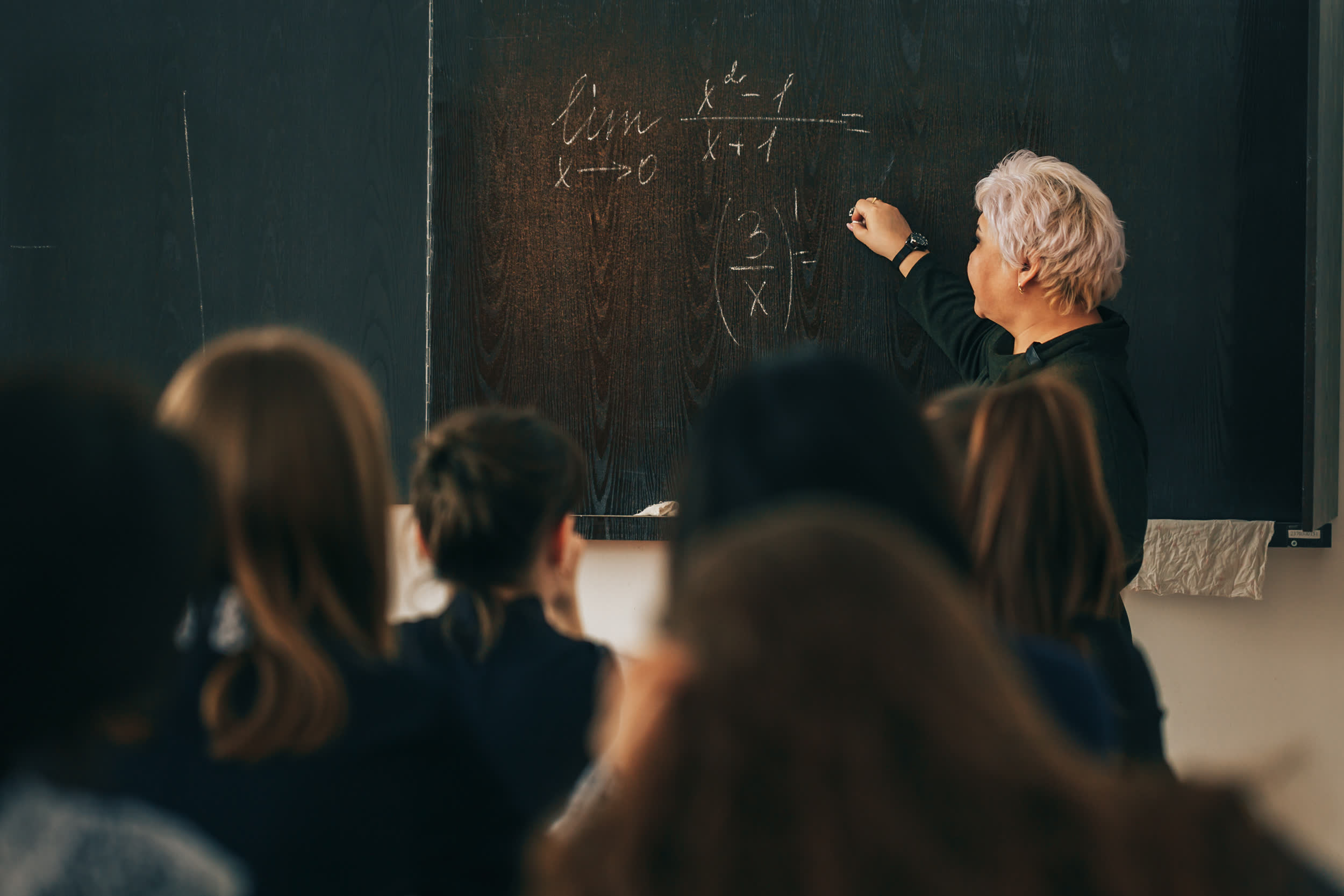 Professora escrivint en una pissarra davant d'una classe en una aula fosca