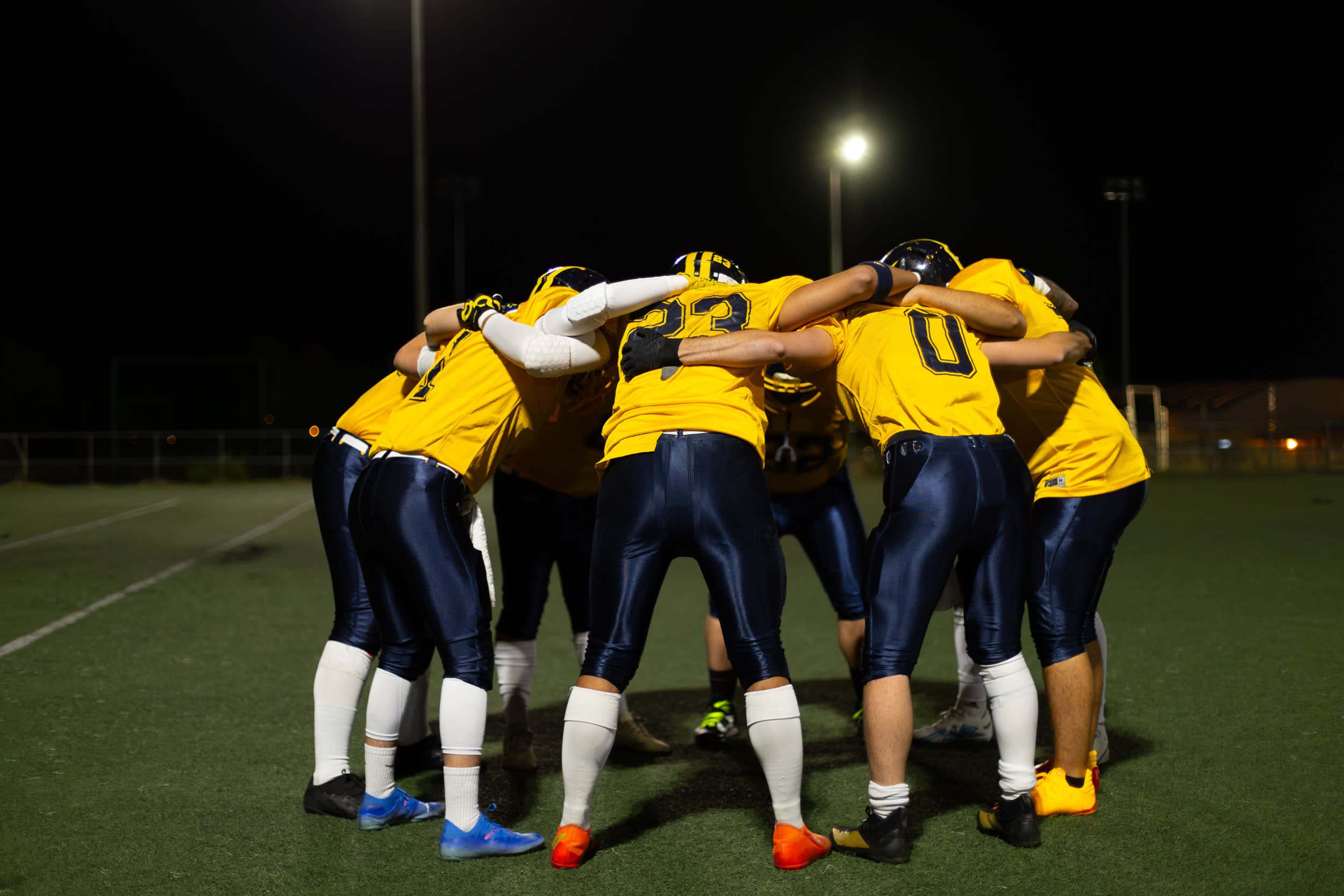 Sportmannschaft im Kreis auf einem Spielfeld unter Flutlicht bei Nacht